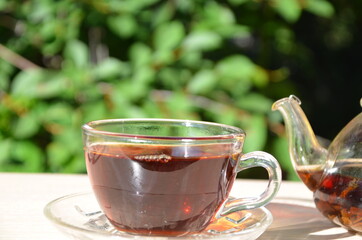 A girl pours tea from a transparent teapot into a transparent cup against a background of green foliage Good morning, outdoor cafe, energy boost. Tea being poured into glass tea
