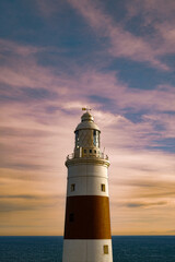 Vertical shot of a tall lighthouse with a pink cloudy sky background