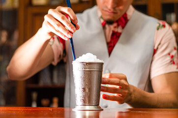 Bartender preparing delicious mint julep cocktail at table.