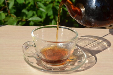 A girl pours tea from a transparent teapot into a transparent cup against a background of green...
