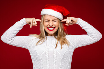 Stock photo of pretty woman with blonde hair in white sweater and Santa hat plugging her ears with hands