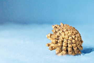 Christmas decoration gold pine cone lying on a blue snowy background.