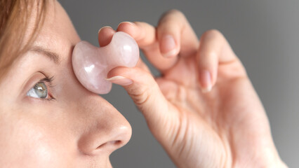 Woman massaging forehead with beauty device made from rose crystal quartz. Massage tool for facial lymphatic drainage. Self beauty care at home