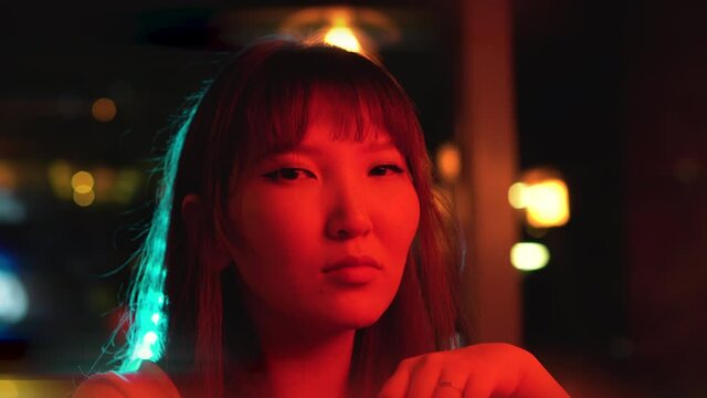 Portrait of a young beautiful Asian woman against the background of neon lights. Reflection of neon hieroglyphs in sunglasses.