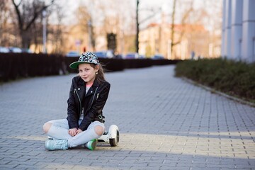 Shy young girl in a cap is resting sitting on a hoverboard.