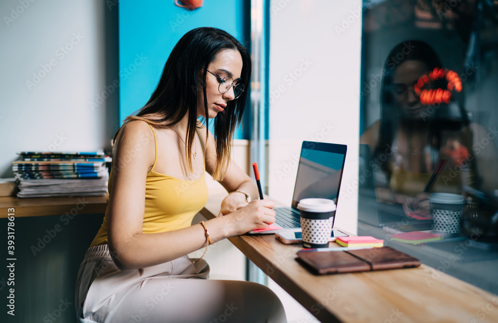 Poster skilled female copywriter in classic eyeglasses writing informative notes while connecting to 4g wir