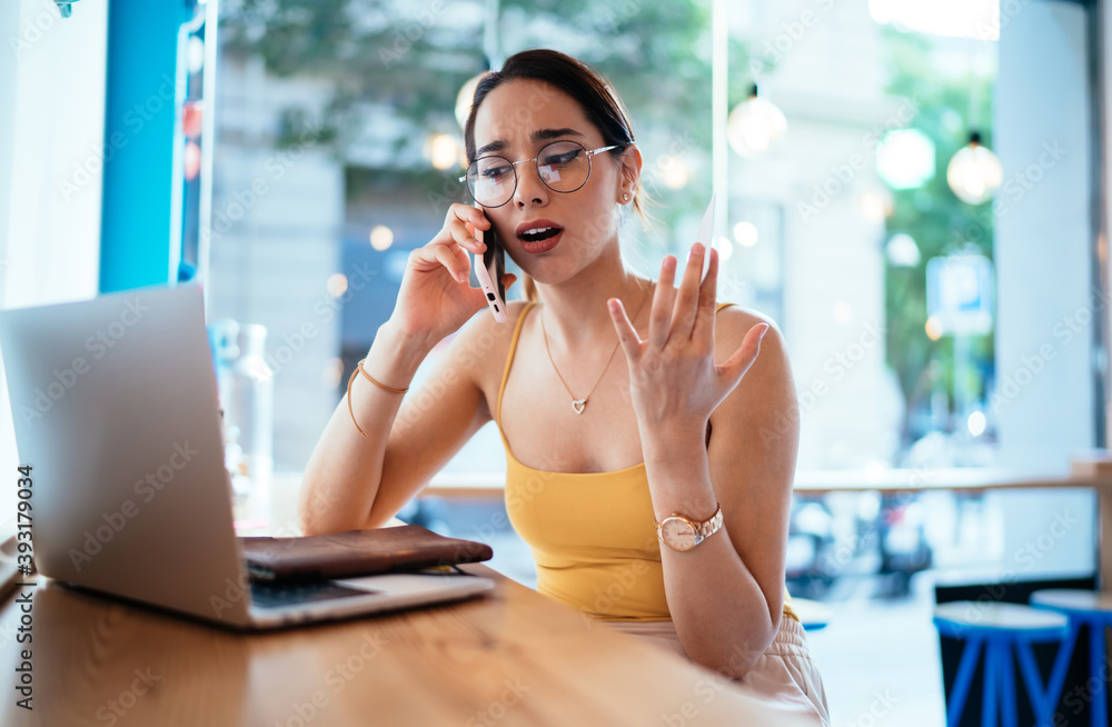 Poster unhappy female freelancer solving problems during smartphone conversation using laptop computer for 