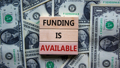 Wooden blocks with concept words 'funding is available' on beautiful background from dollar bills....