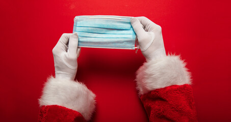 Santa Claus hands holding a coronavirus surgical face mask. Covid Christmas