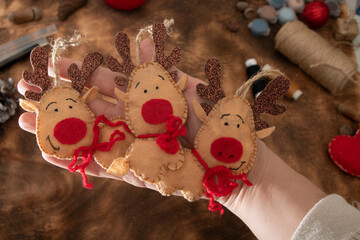 Holding a handmade Christmas tree toy. Felt toy - deer on wooden background. Ready for holidays.