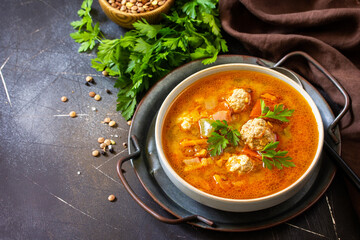 Tomato-lentil soup with meatballs and vegetables on a dark slate table top. Copy space.