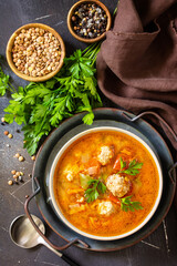 Tomato-lentil soup with meatballs and vegetables on a dark slate table top. Top view flat lay background.