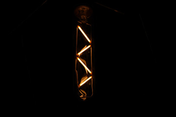 Close up image of a vintage filament light bulb glowing in the dark with detail of fingerprints on it