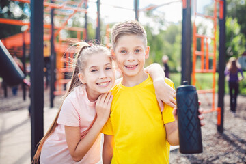 Fototapeta na wymiar Sportive friends. Brother and sister standing together at street city gym. Children athletes hug smile during workout training. Twins boy and girl posing on playground. Physical development education