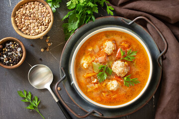 Tomato-lentil soup with meatballs and vegetables on a dark slate table top. Top view flat lay background.