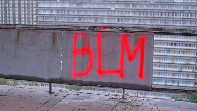 Man in hood writes BLM with spray paint on the wall . Footage of making protest graffiti.