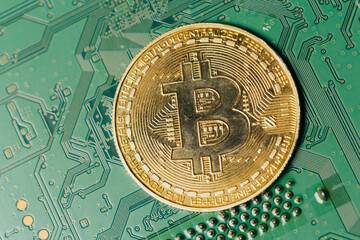 Gold coins with bitcoin symbol on green motherboard.