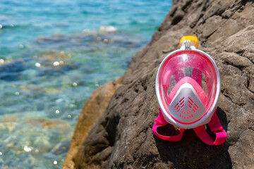 A full-face mask for snorkeling lies on the beach. Sand and water. Place for text. Pink for...