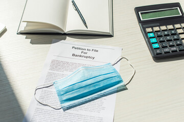 Medical mask on petition for bankruptcy near blank notebook and calculator on white textured...