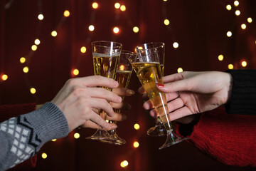 Unrecognizable group of friends at a Christmas party making a toast, lights at the background. Christmas celebration.