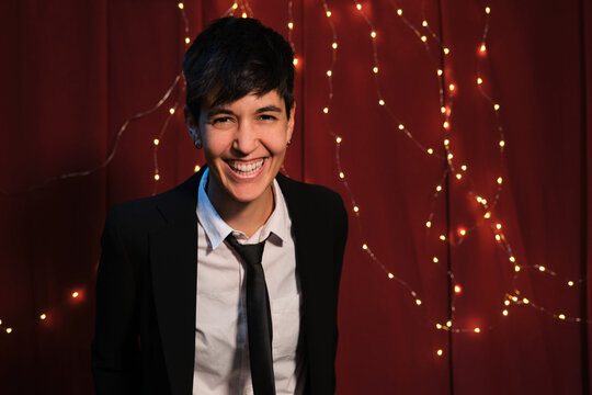 Pretty Lesbian Woman Laughing, Wearing Suit And Tie With Lights Background. Christmas Celebration.