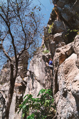 a woman climbs on a vertical rock wall on the blue sky background