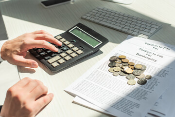 Cropped view of businessman counting on calculator near coins on petitions for bankruptcy on table