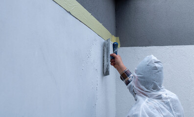 worker in white protective coveralls is plastering the wall