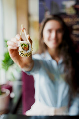 Happy girl is giving sushi to you in japanese restaurant. Young girl is holding sushi by chopsticks...