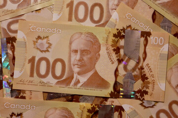 Canadian hundred dollar bills are scattered on a surface. 