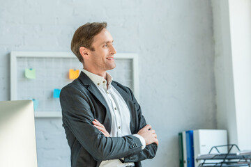 Smiling businessman with crossed arms looking away with blurred office background