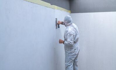 worker in white protective coveralls is plastering the wall