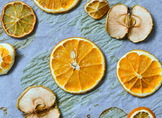 Fototapeta na wymiar dried slices of orange and lemon as well as apples on parchment, decoration for the new year, fruit chips.