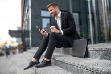 Elegant male businessman sitting on the steps and texting