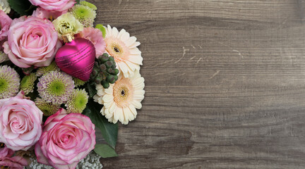 bouquet of roses on the left with a pink heart bauble on wooden background  - copy space