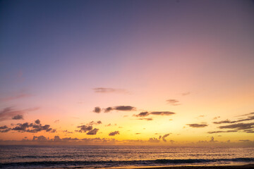 Obraz premium Dramatic sea shore sunset with sun setting down at the cloudy skyline with orange and vivid blues.