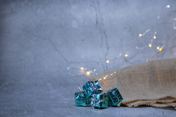 Blue 4 gifts with shiny packaging on a gray background with burlap and small yellow lanterns.