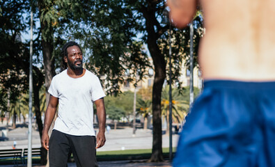 Afro man with dreadlocks trains a group of athletes in the street. Personal trainer