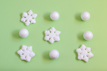 White decorative snowflakes and balls on the light green background. Top view, pattern photo.