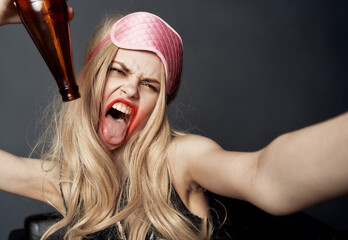 Drunk woman with a bottle of beer on a gray background gestures with her hands and bright makeup