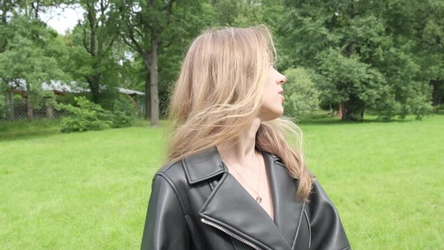 Beautiful young blonde girl walks in a summer green park, posing, looking at the camera and straightens her hair