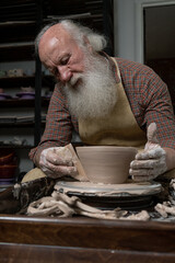 Old male potter. High angle of craftsman working on pottery wheel while sculpting from clay pot in workshop. Focus on arms. Concept of ceramic art