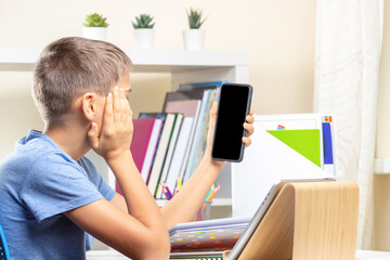 Teenage boy distracting from online lesson and playing video games, scrolling phone, texting on...