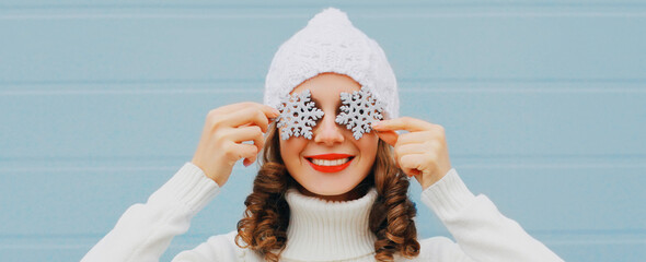 Winter portrait close up of happy smiling woman holding snowflakes covering her eyes wearing a...