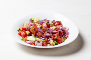 vegetable salad with  red onion, tomato, cucumber, avocado, dill, sumach, paprika, olive oil  in white bowl on wooden table