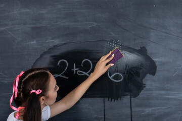 A standing teenager wipes a dirty school blackboard with a wet sponge. The school blackboard is...