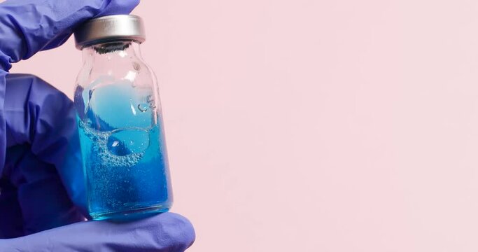 Vaccine development during a pandemic. Doctor hand in medical protective gloves holds the vaccine fluid bottle against pink background.