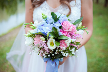 The bride holds a beautiful pink blue and green wedding flowers bouquet in her hands on green background. Detail of wedding day flowers