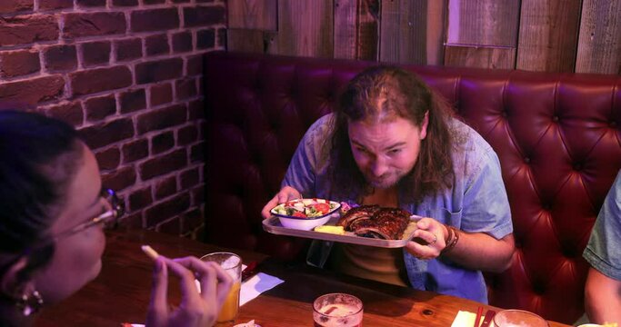 Man holding plate of bbq ribs in restaurant with friends