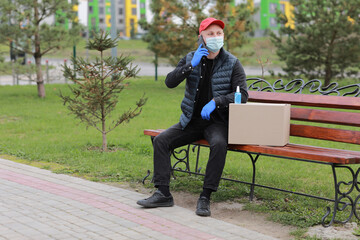 Fototapeta premium Delivery man in red hat, protection mask and medical rubber gloves with parcels using smartphone to sending to customer. delivery service during coronavirus. Online shopping